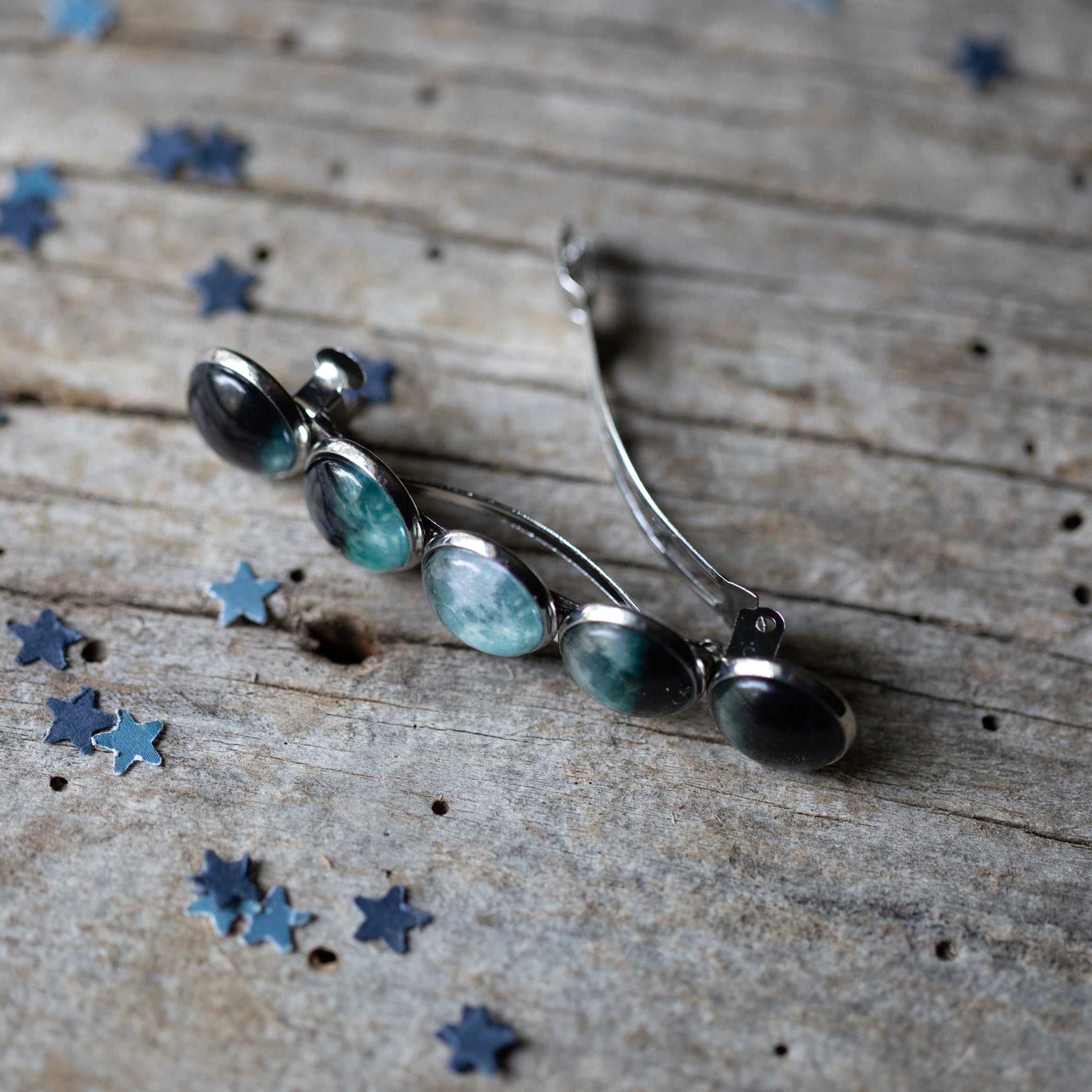 Silver brooch with green gemstones on a wooden surface with star-shaped objects.