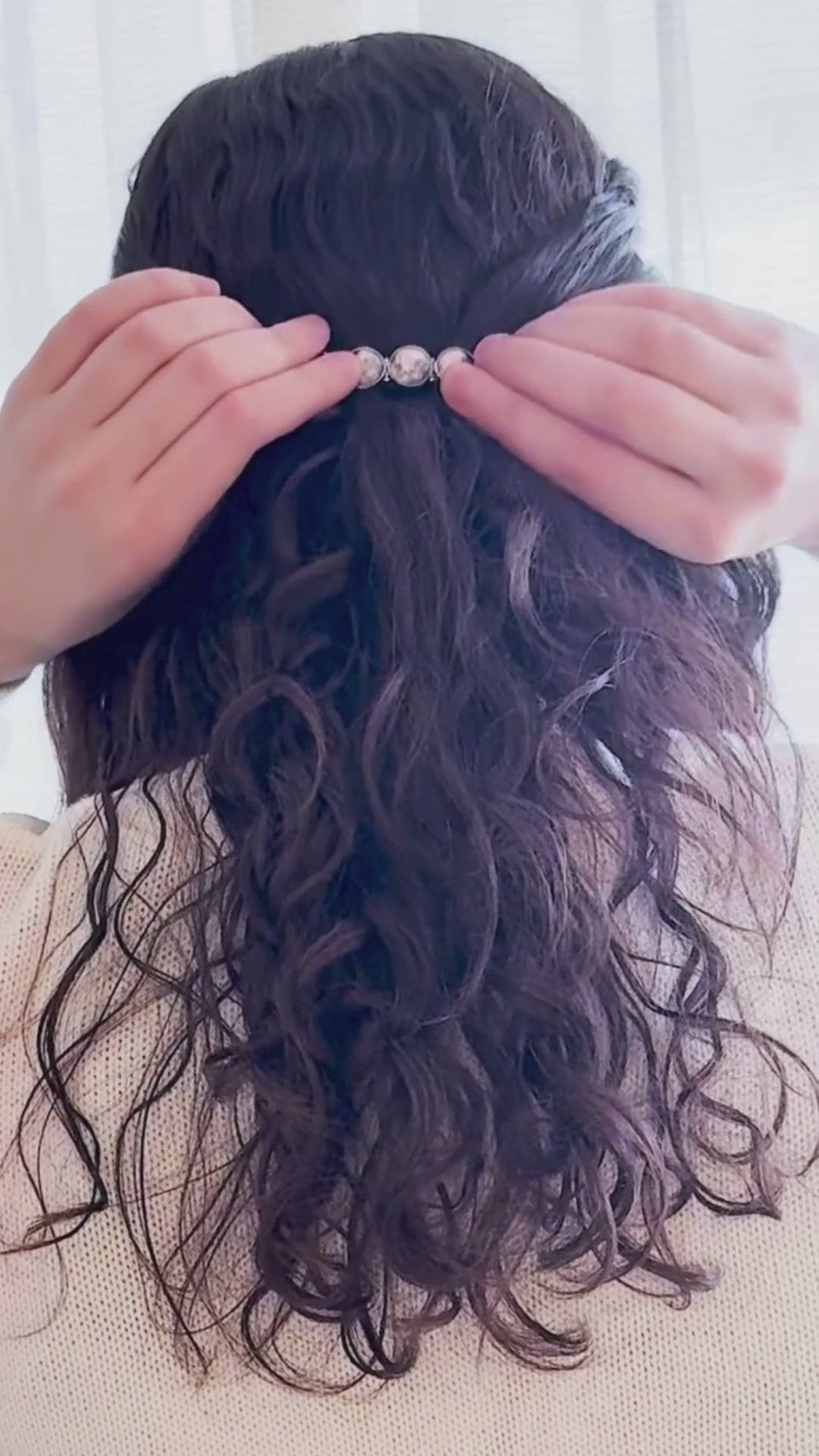 Dark brown hair with a hair clip held by hands against a neutral background